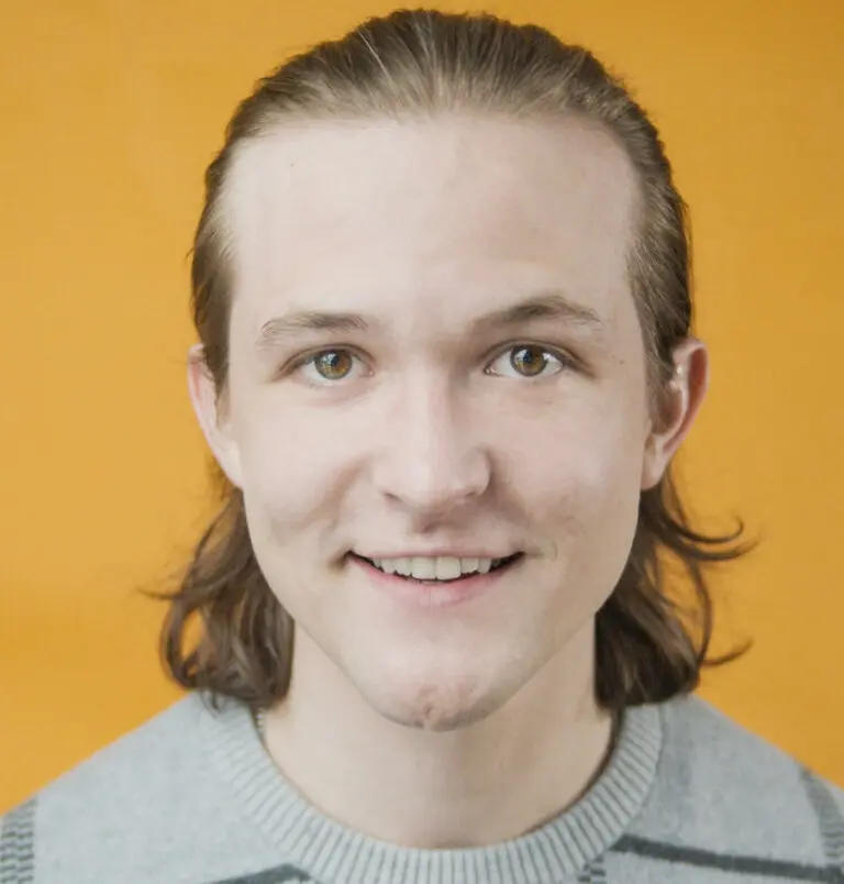 Actor Danny Irizarry wearing a gray sweater in front of an orange background.