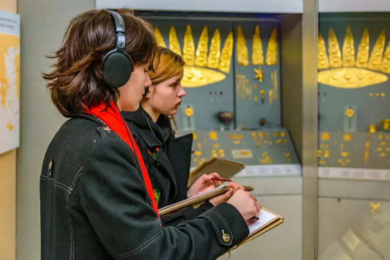 An actor researching her character in a museum surrounded by ancient gold artifacts.