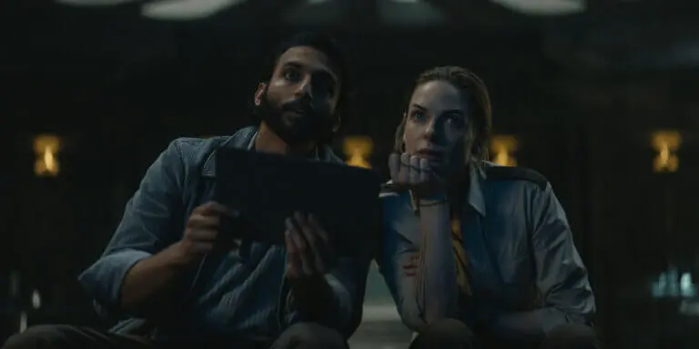 Avi Nash and Rebecca Ferguson holding a notepad staring.