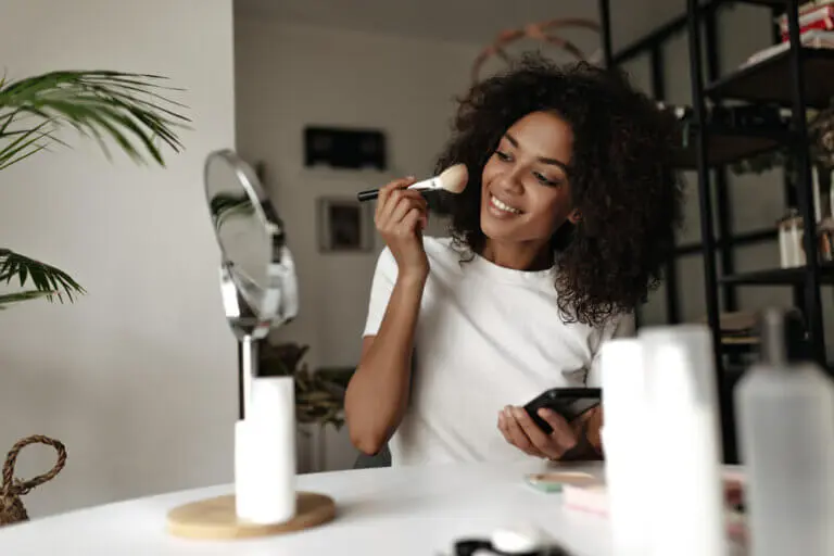 African American woman applying makeup and smiling.