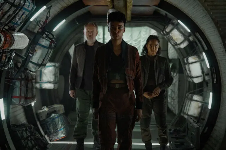 Jared Harris, Leah Harvey and Lou Llobell walking down a futuristic hallway.