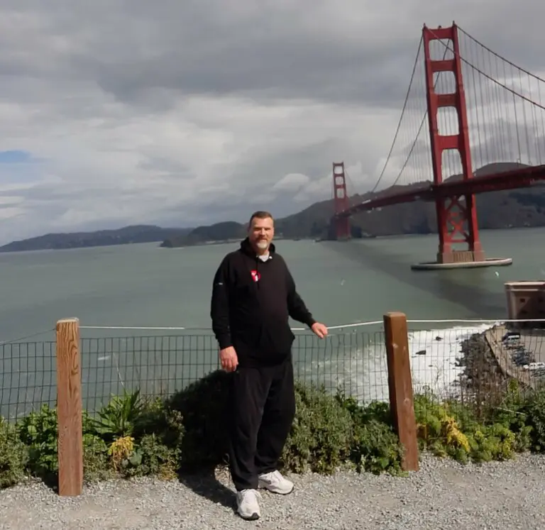 Tim Swain in a track suit smiling by the Golden Gate Bridge.