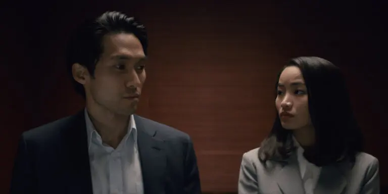 Jin Ha and Anna Sawai in "Pachinko" wearing business attire and looking nervous in an elevator.