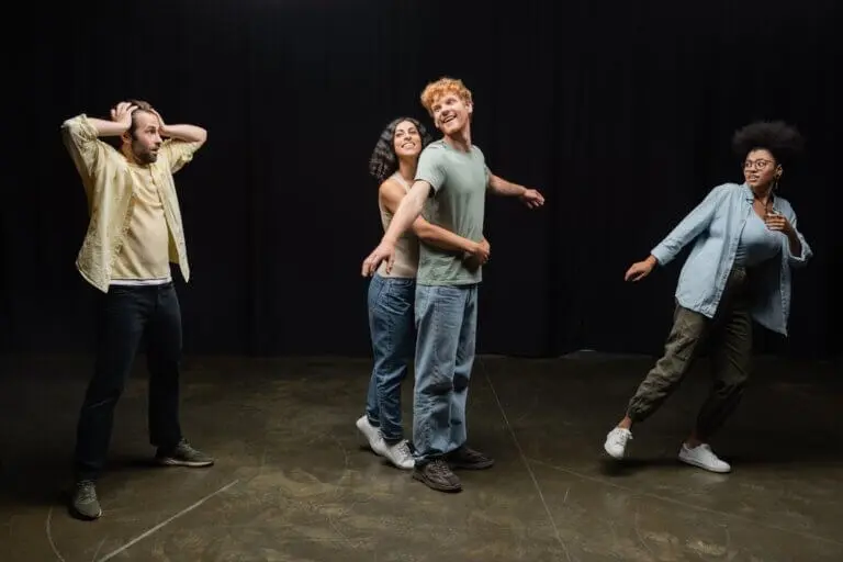 Four diverse actors running through a scene in rehearsal. Two look surprised while two are embracing.