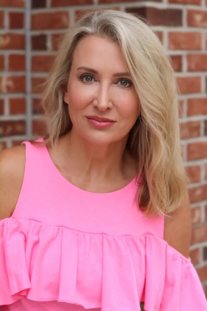 Amy McKillop smiling in front of a brick wall outside in a pink dress.