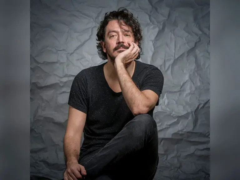 Director/writer Tolga Karaçelik in a black shirt and jeans looking stoic by a gray wall.