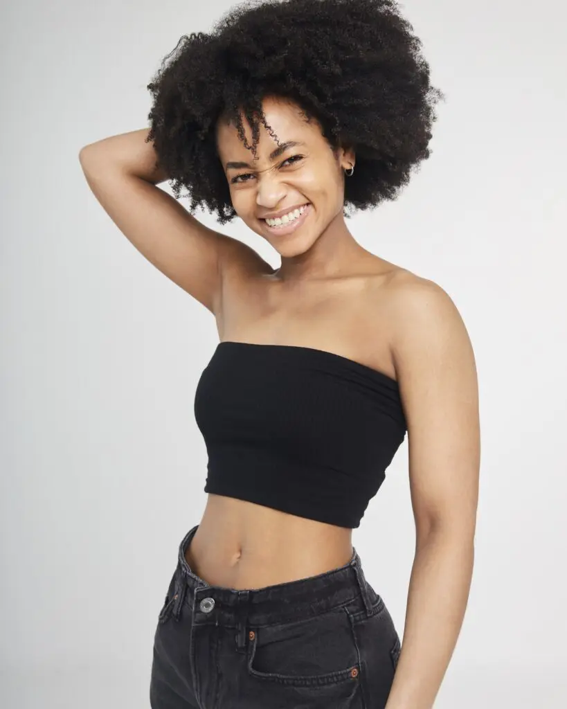 Sarah Murray smiling with her arm behind her head in black jeans and a black crop top.