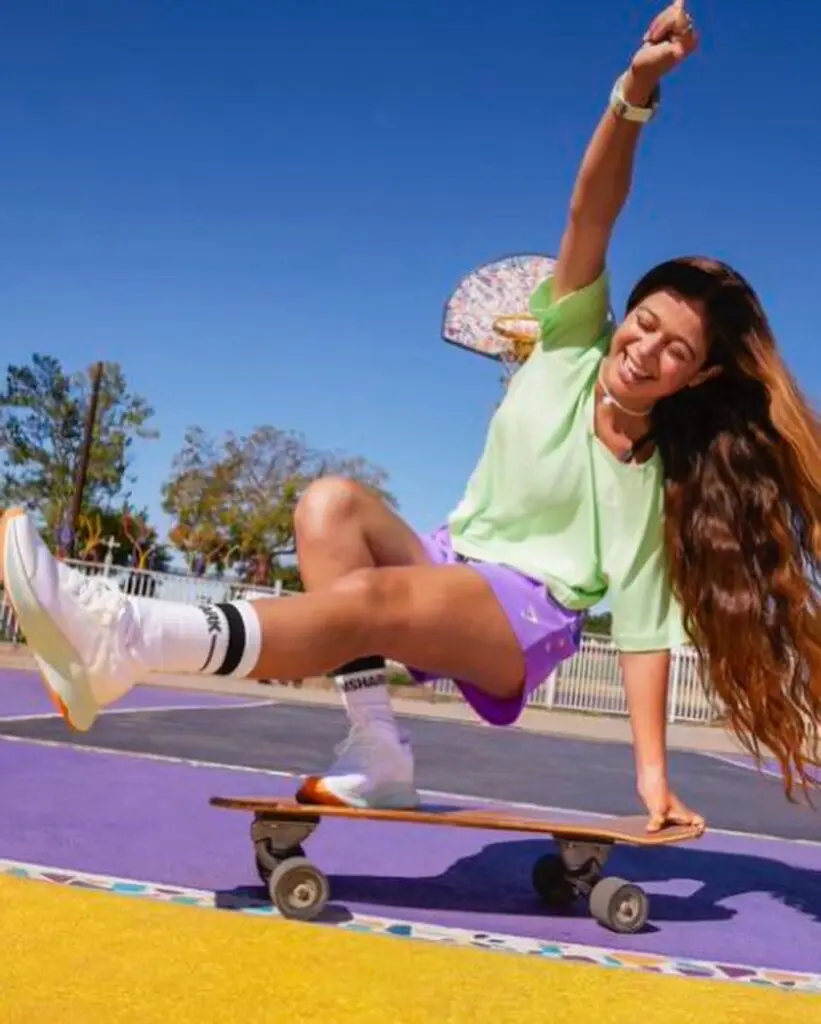 Pauline Sala on a skateboard, leg kicked out and arm in the air at a skatepark.