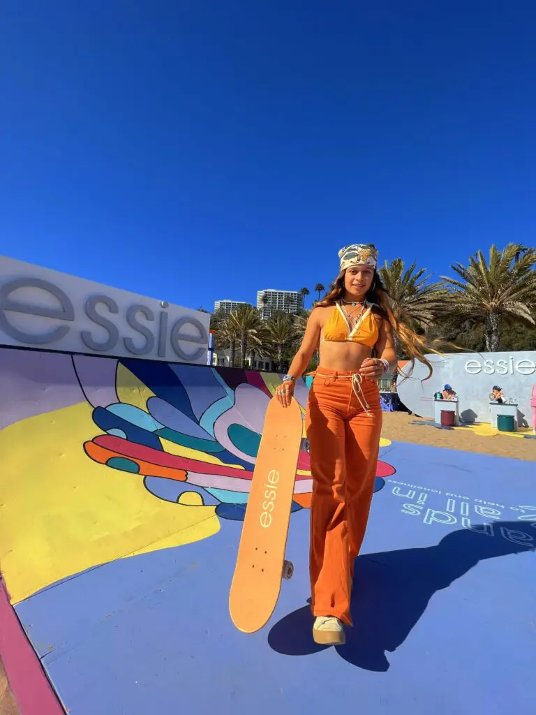 Pauline Sala at the Venice Beach skatepark with a board in hand in 70s style clothing.