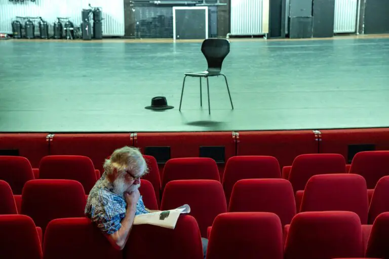 Actor sitting in an empty theater researching his character. A chair and hat are on am otherwise bare stage.