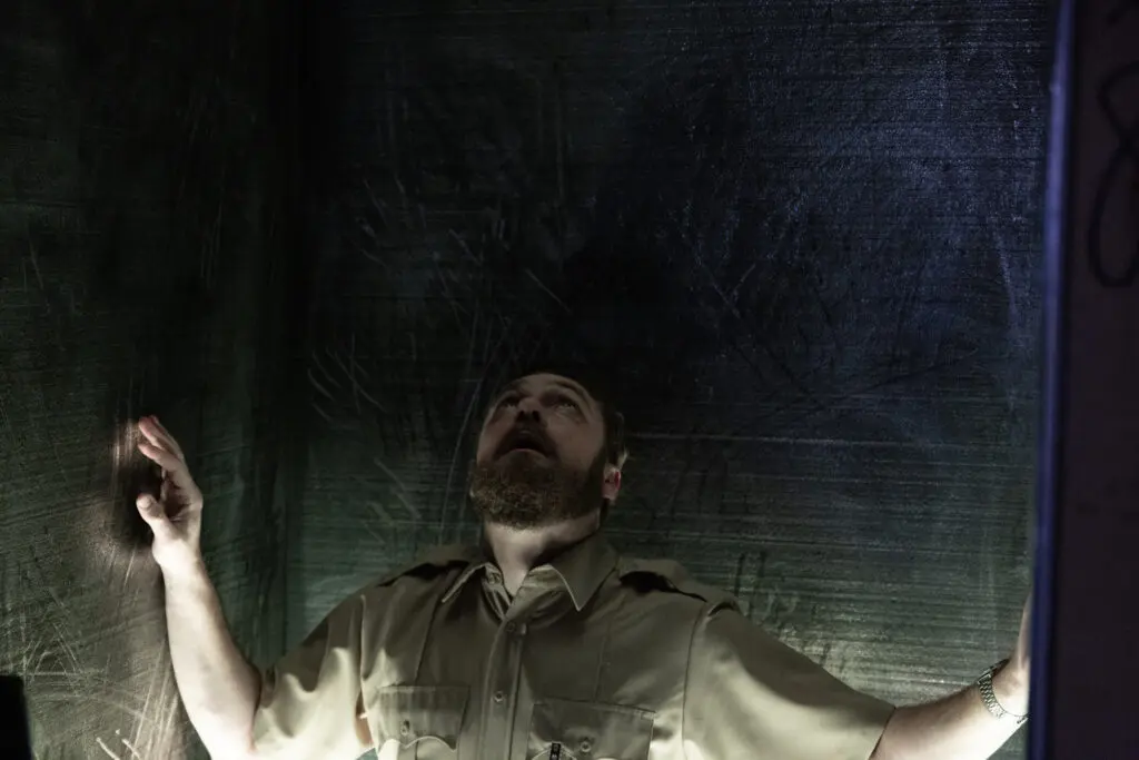 Ross Marquand terrified in an enclosed steel pod with scratch marks on the walls.