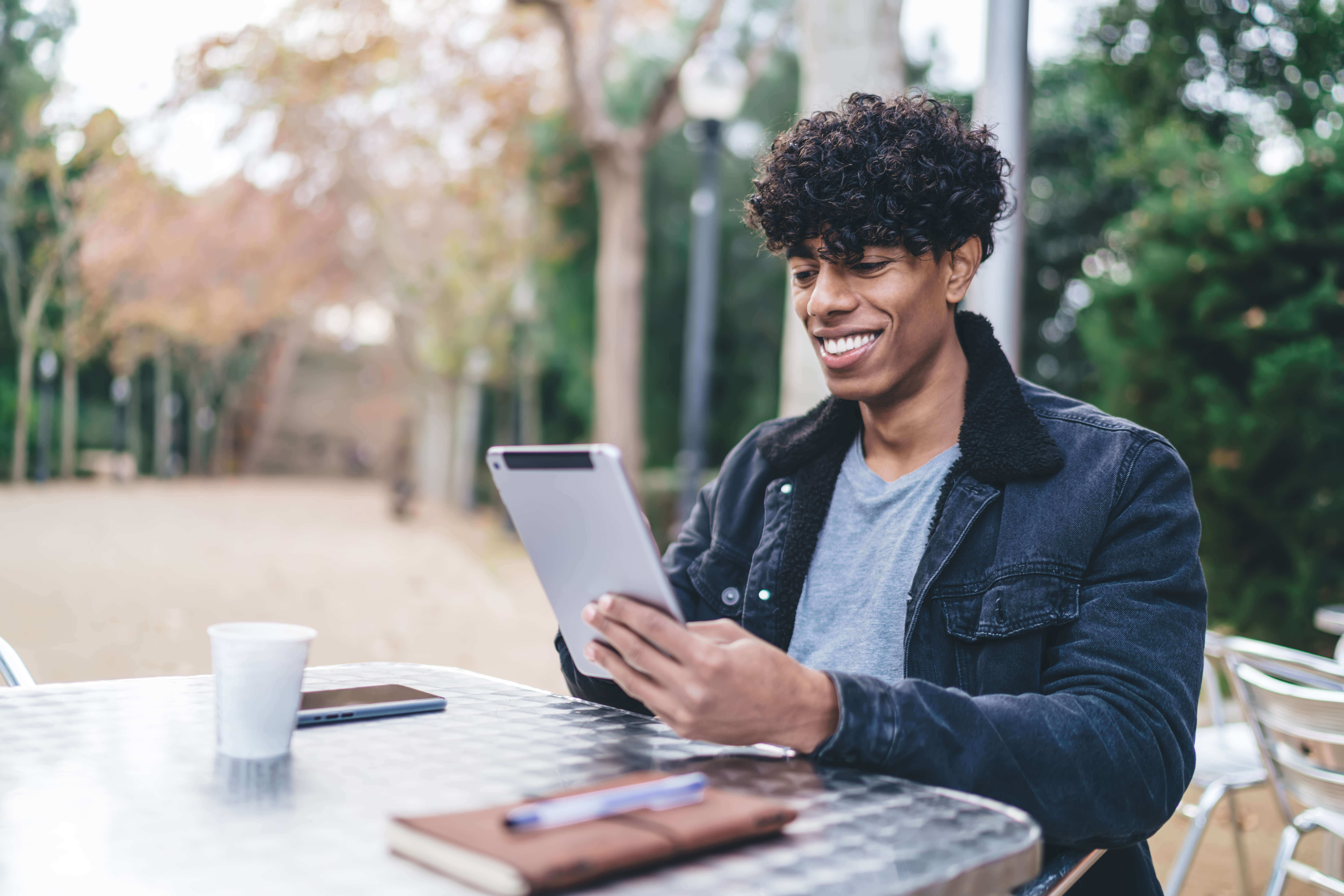 Good looking male blogger spending leisure day in street cafeteria and watching video review on website connecting to public wireless internet for online networking, positive man reading comments