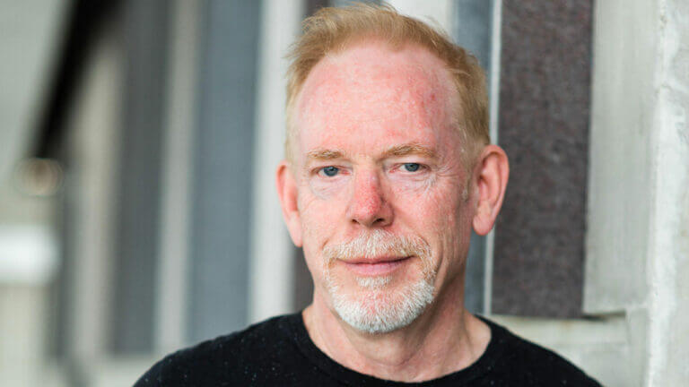 Tom Keegan, a video game performance director. outside in front of a building in a black shirt.