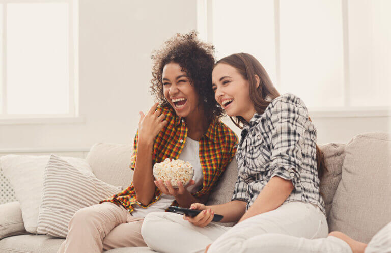 Two actors sitting on a couch watching some of the series streaming in March on our list.
