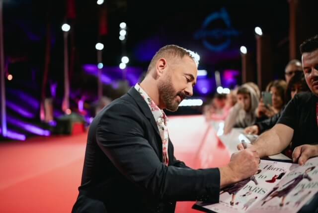 Mrs. Harris Goes to Paris director Anthony Fabian signing pictures on the red carpet.