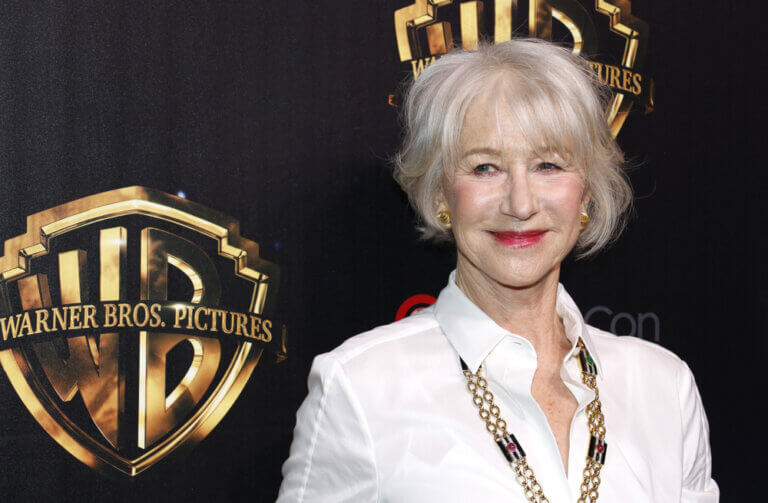 Helen Mirren outside of an event smiling in front of a Warner Brothers backdrop.