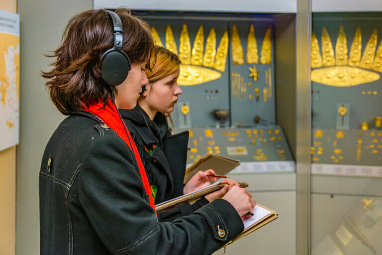 An actor researching her character in a museum surrounded by ancient gold artifacts.