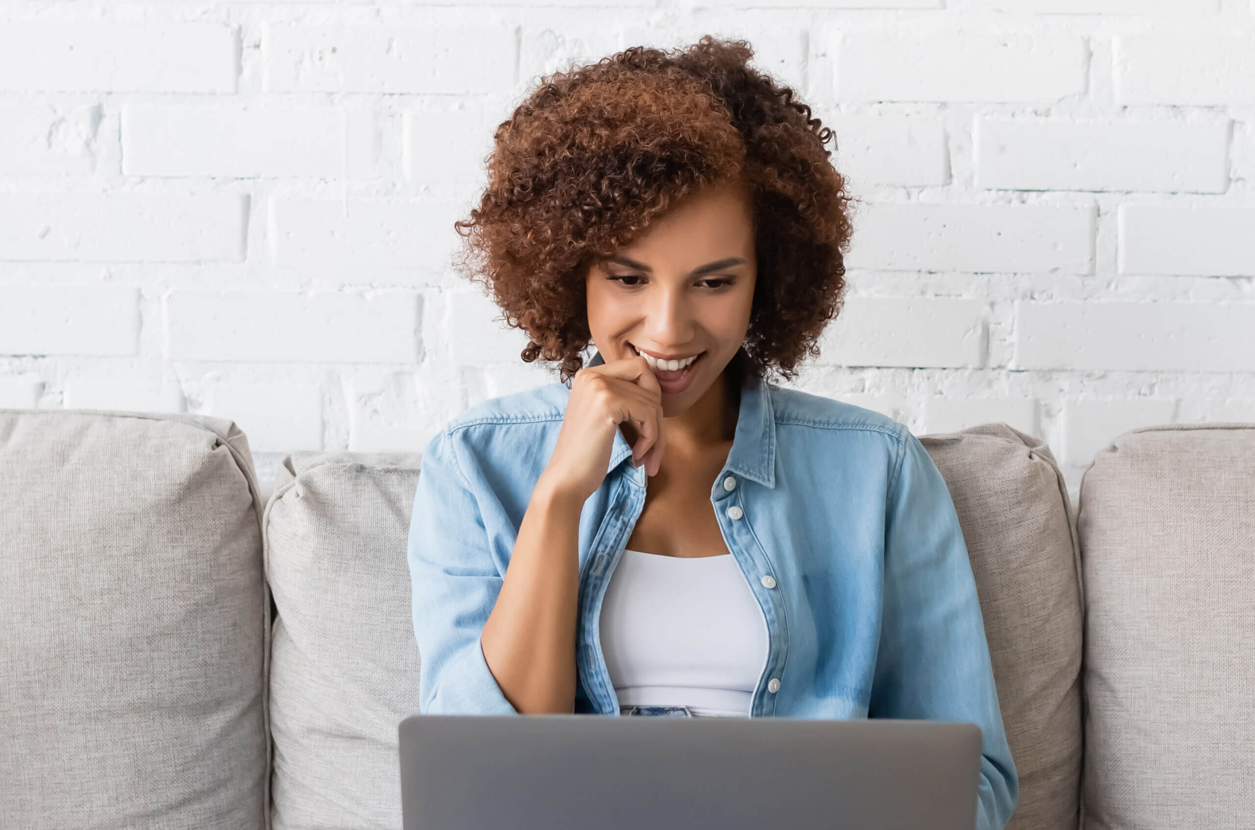 A casting director with curly hair on her laptop on a gray couch.