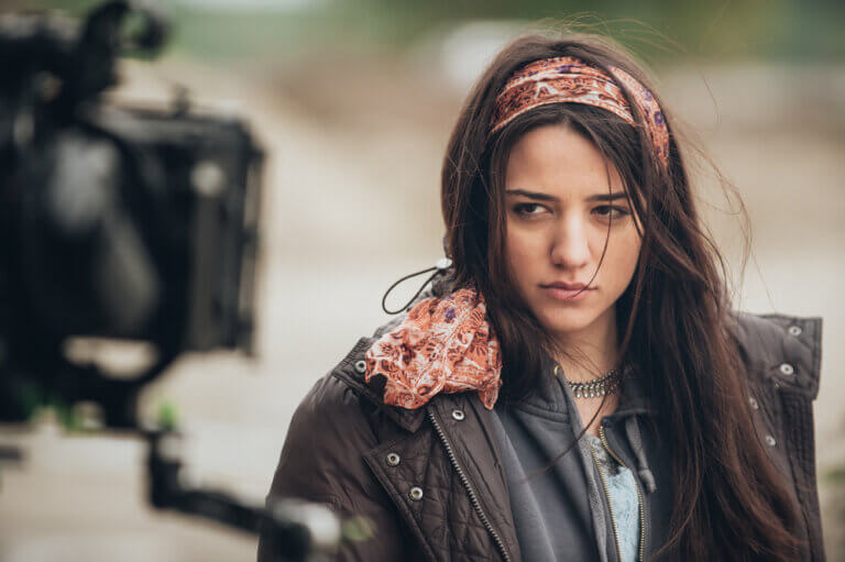 An actress wearing a leather jacket filming a dramatic close-up scene outdoors.