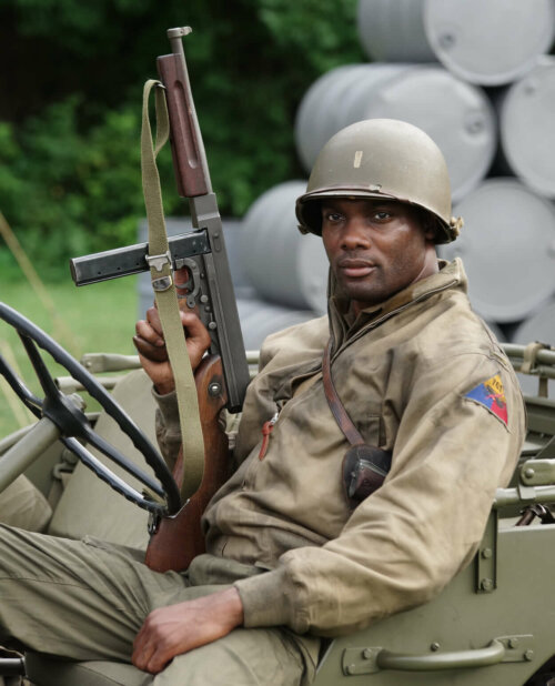 Actor Hiram A. Murray wearing army fatigues and a helmet in a car holding a gun.