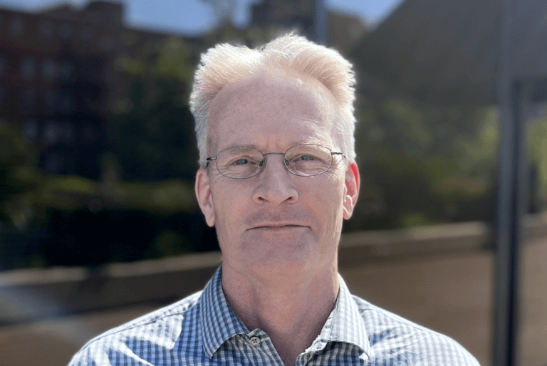 Talent Systems CFO Jim Arth outside smiling wearing a blue and white buttoned down shirt.
