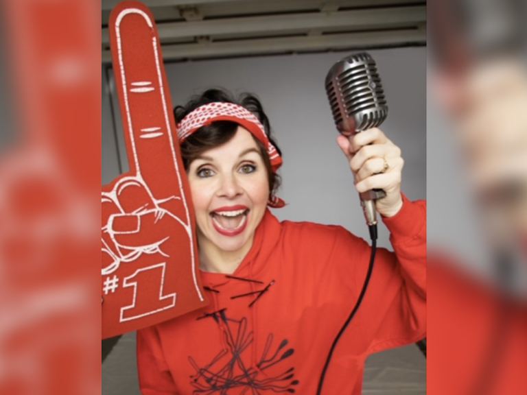 Audrey Moore with a red hoodie, microphone in hand and a foam finger smiling.