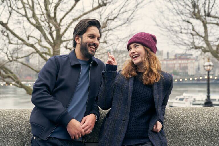 Actors Shazad Latif and Lily James outside during a foggy winter day in the film What's Love Got to do With it?
