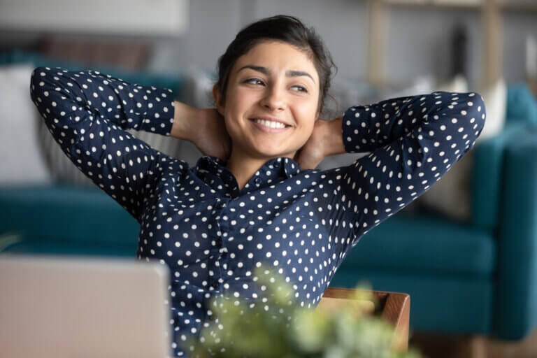 A girl in her 20s wearing a blue shirt relaxes at her desk at home.