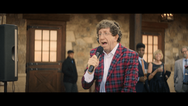 Actor Dan Jablons in a red and blue plaid suit singing.