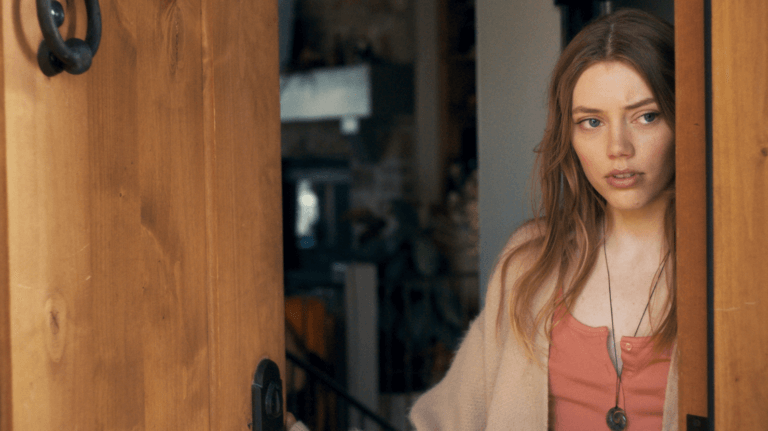 Grace Van Dien opening a door with an intrigued look.