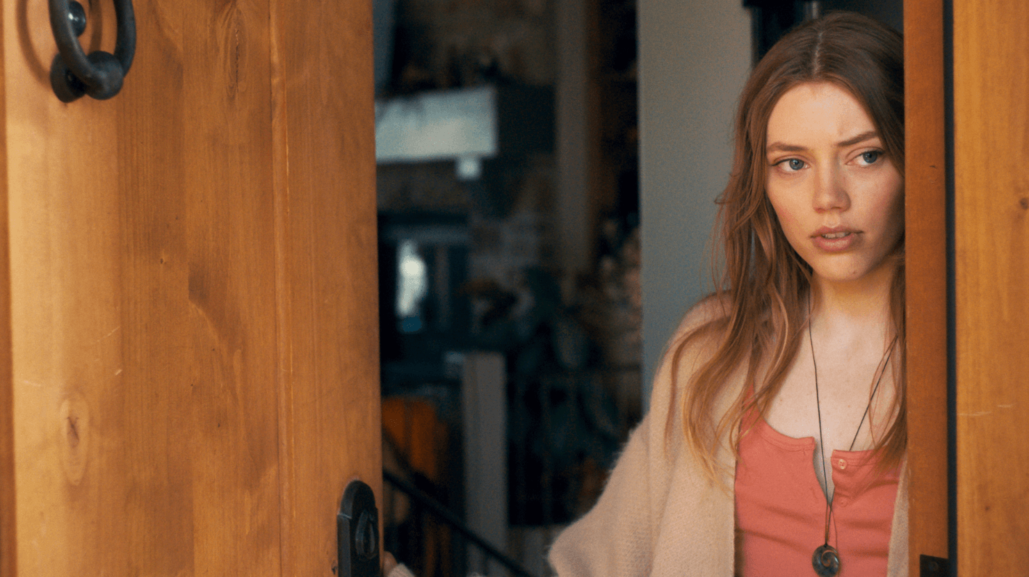 Grace Van Dien opening a door with an intrigued look.
