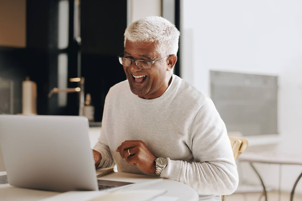 A happy Indian senior at home on his laptop smiling.