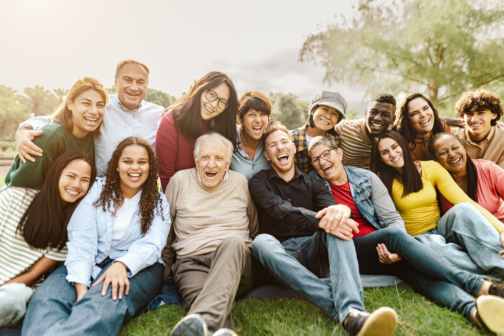 A diverse and multigenerational group of people smiling and hanging out in the park.