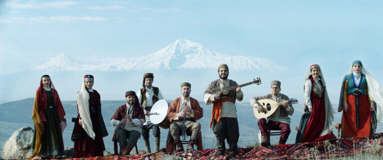 Armenians wearing traditional clothing playing music on a mountain.