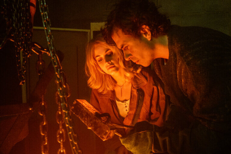 Stefanie Martini and Tom Cullen staring at a gold bullion in a dimly lit room.
