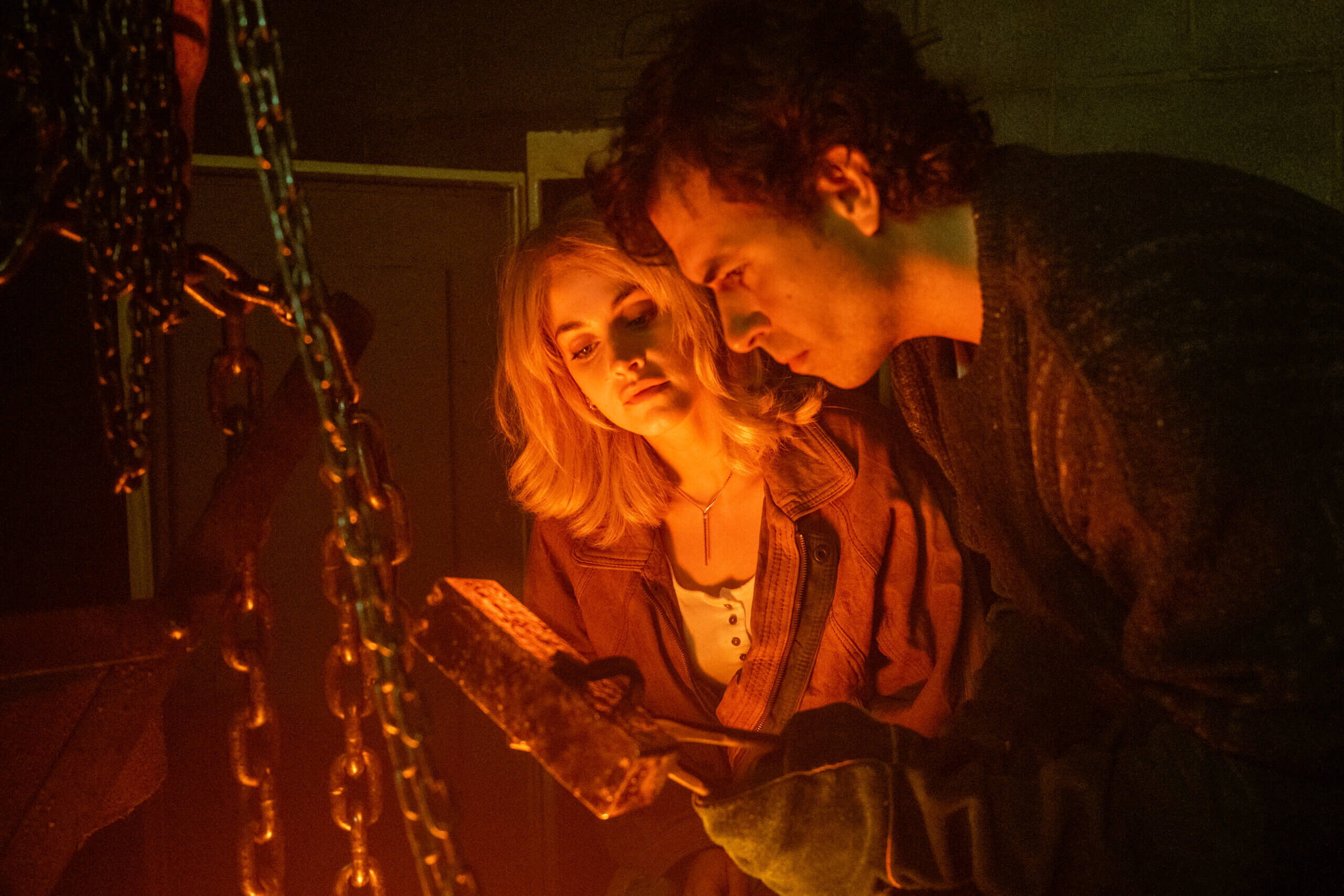Stefanie Martini and Tom Cullen staring at a gold bullion in a dimly lit room.