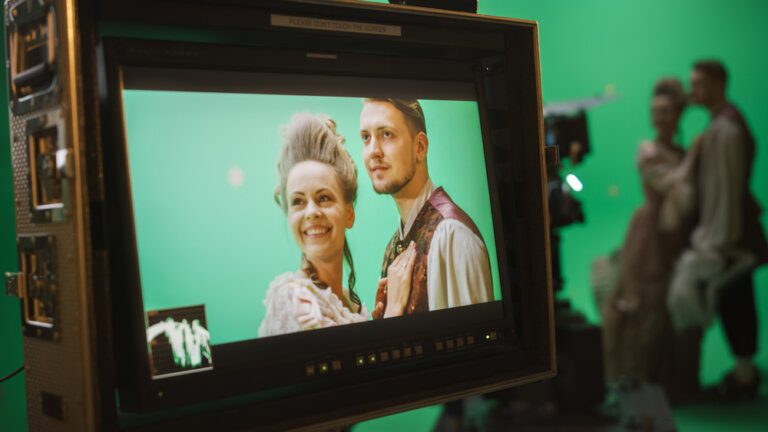 Actors on a directors screen in old Victorian costumes. A green screen is behind them.