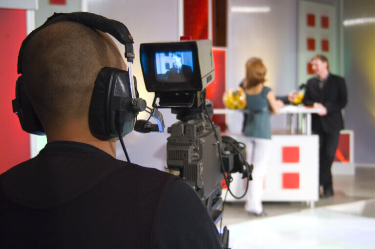 Cameraman , on set with two actors filming a tv commercial.