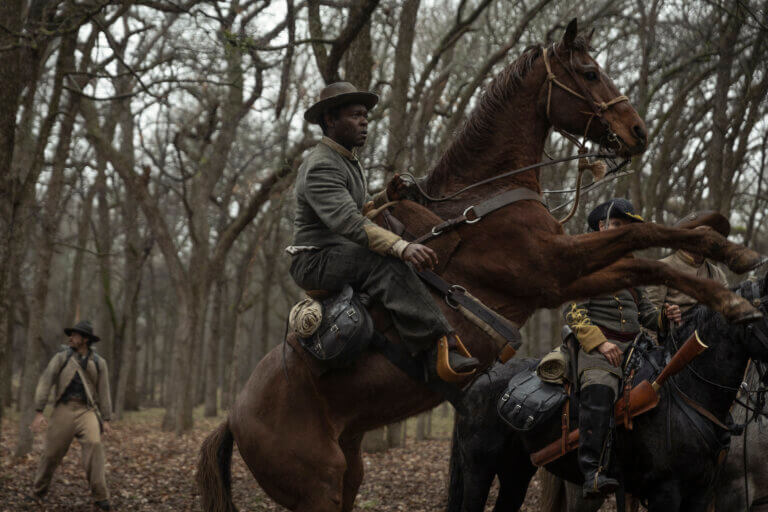 Actor David Oyelewo in coyboy gear riding a horse in the woods..