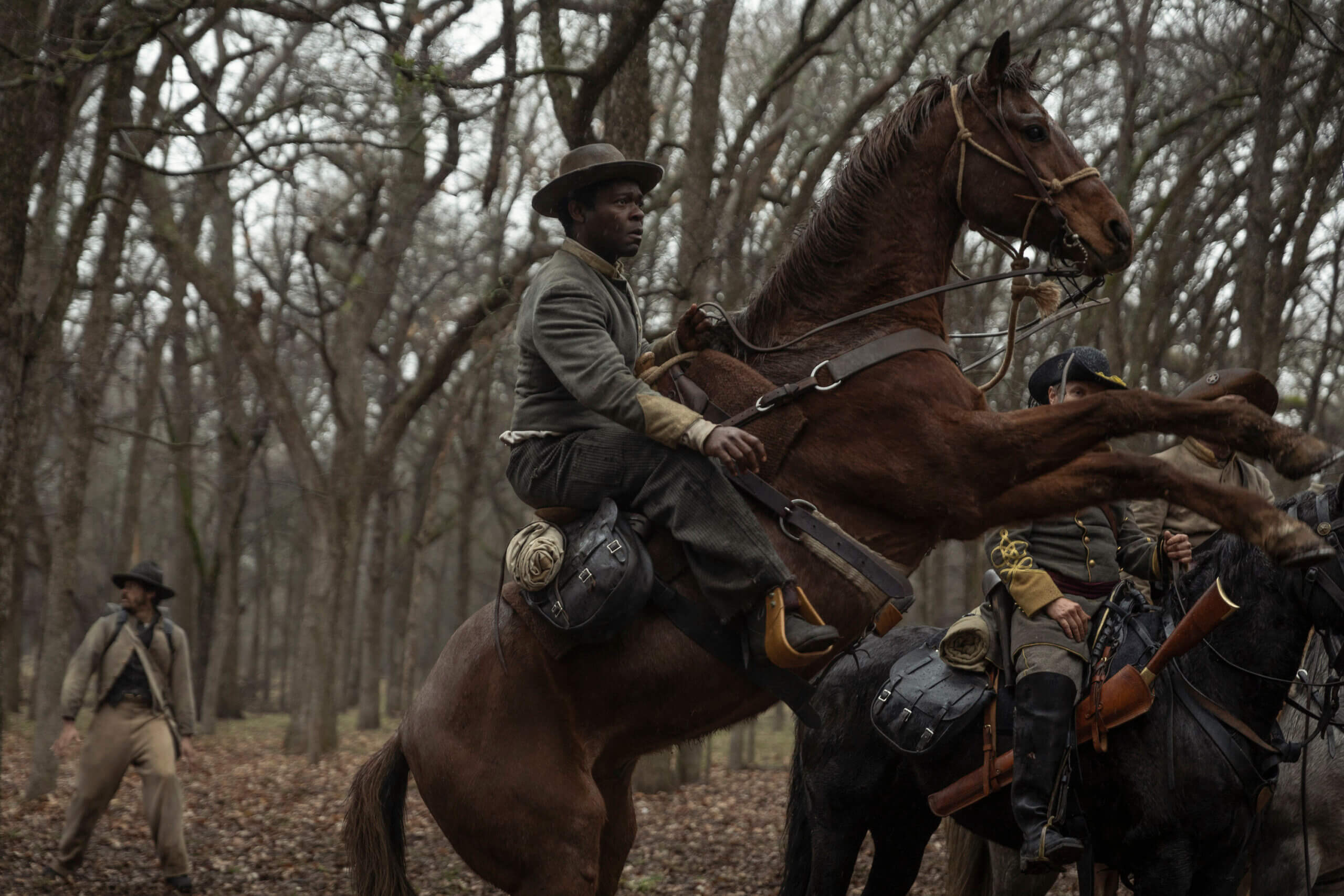 Actor David Oyelewo in coyboy gear riding a horse in the woods..