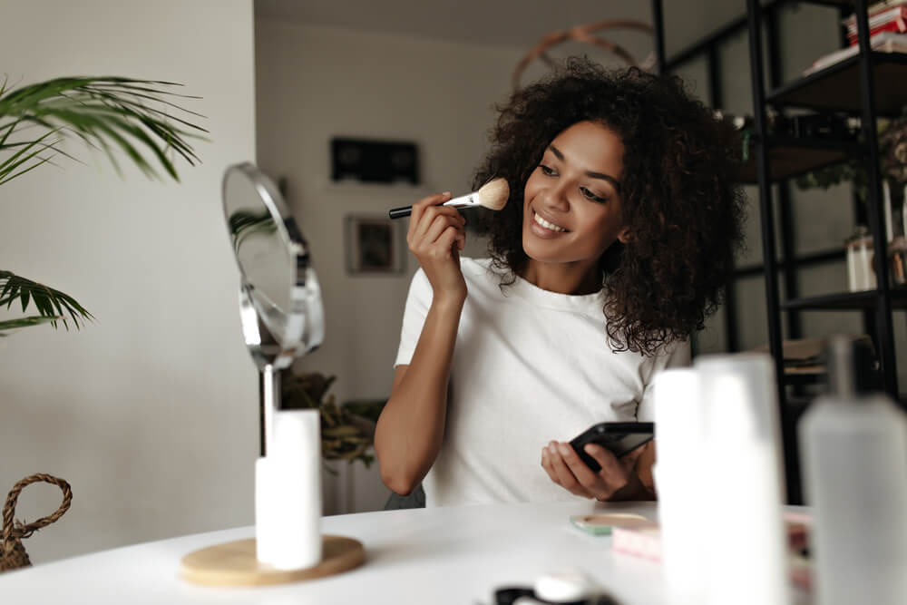 African American woman applying makeup and smiling.