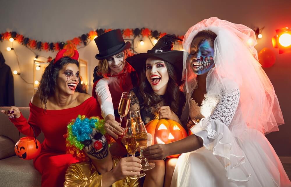 Friends at a halloween party dressed in various spooky costumes having a toast.