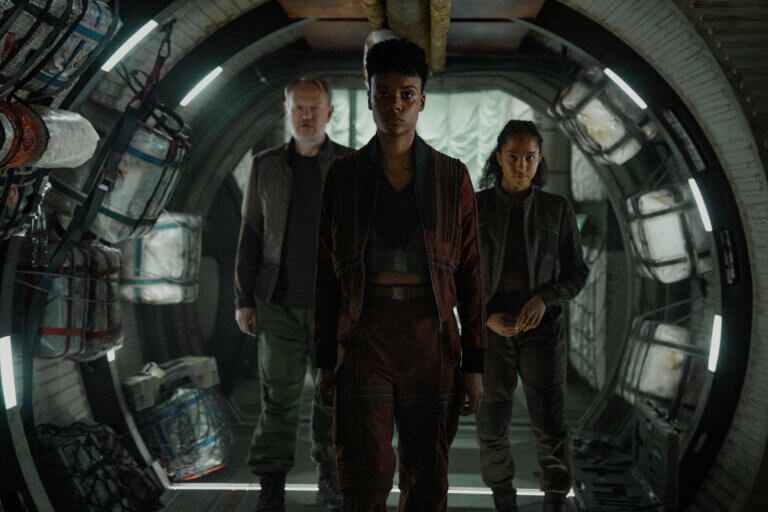 Jared Harris, Leah Harvey and Lou Llobell walking down a futuristic hallway.