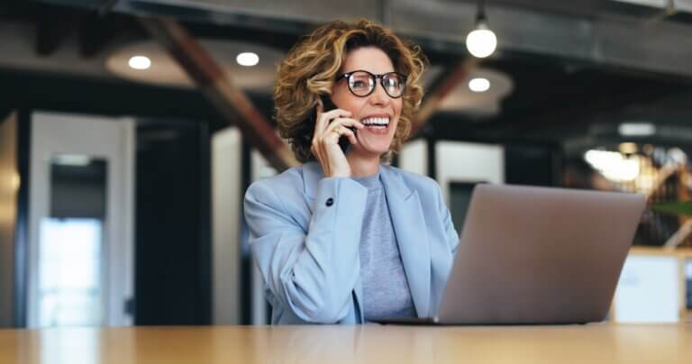 Business woman on her phone and laptop smiling.