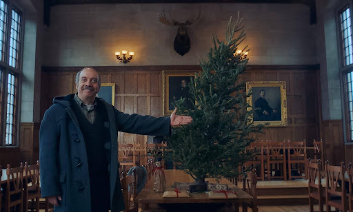 Paul Giamatti presenting a small christmas tree inside a dining hall.