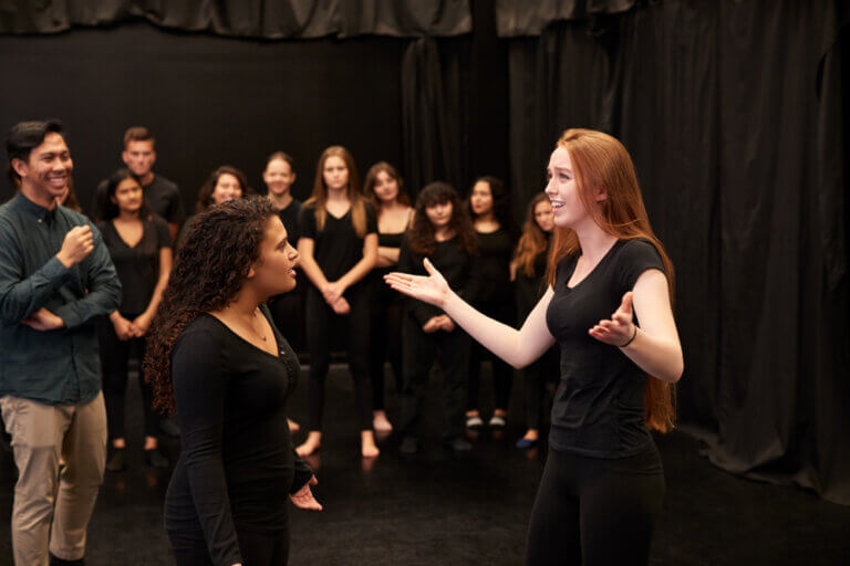 A diverse group of improv students performing an exercise with their teacher.