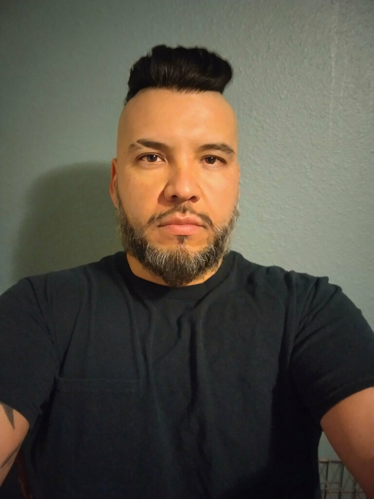 Eduardo Flores taking a selfie in front of a grey background.