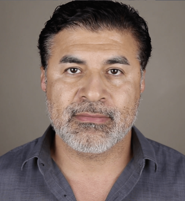 Gerardo Davila smiling in front of a grey background.