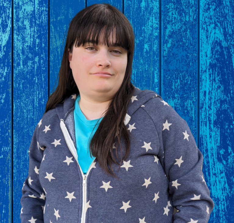 Actor Heather Cowles smiling in front of a blue background.