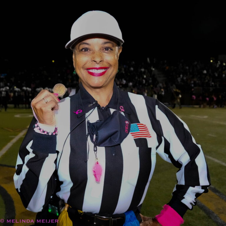 Crystal Nichols in a referee outfit on a football field holding a coin.